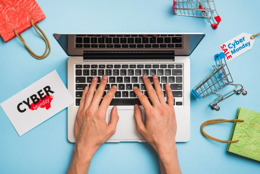 Handen typen op laptoptoetsenbord met boodschappentassen en dummy-winkelwagentje