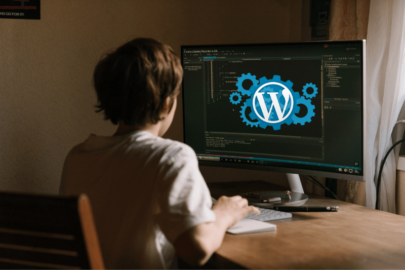 Een WordPress-ontwikkelaar zit aan een bureau en kijkt naar zijn computerscherm met tandwielpictogrammen en een WordPress-logo